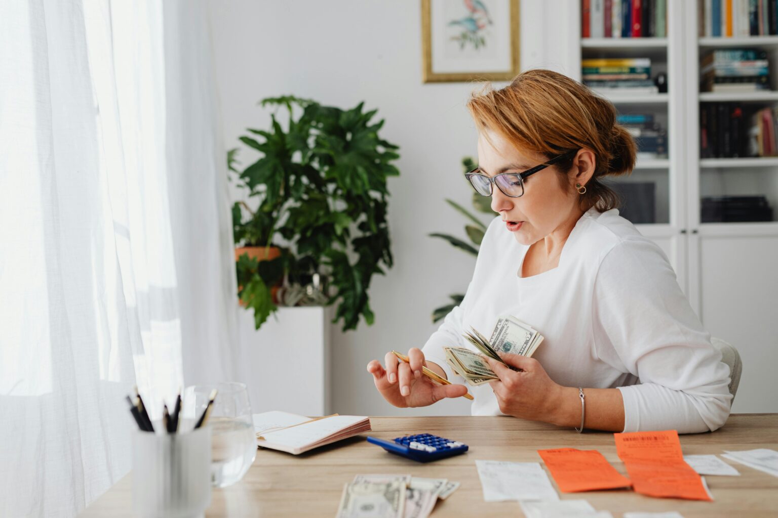 A woman sitting at her desk, counting money for home budgeting management.