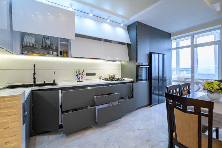 Spacious luxury white and dark grey modern kitchen interior with dining table, most furniture drawers and doors are open